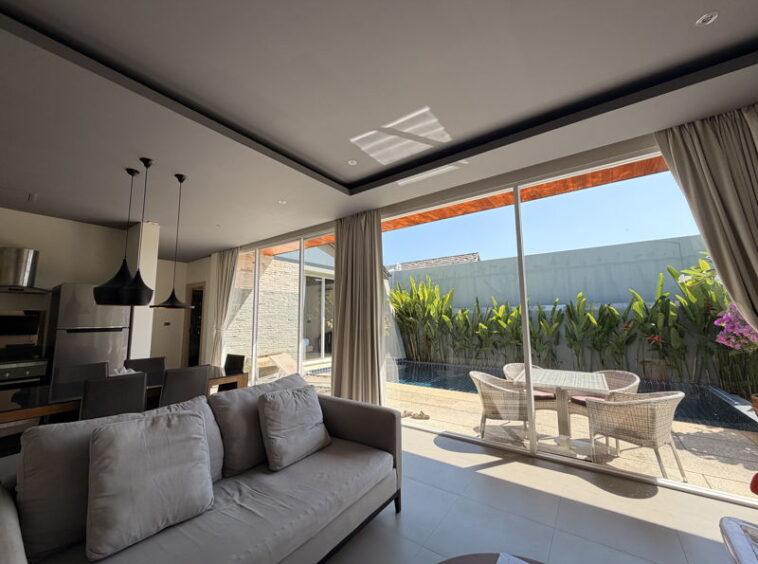 Bright living room with a grey sofa and sliding glass doors opening to a poolside patio and wicker table set.