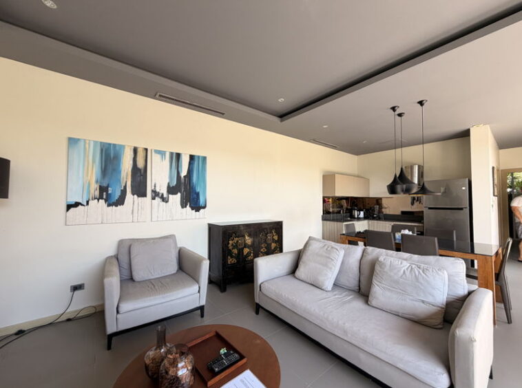 Open-concept living room with two white sofas, a gray armchair, and a round wooden coffee table; abstract blue wall art above.
