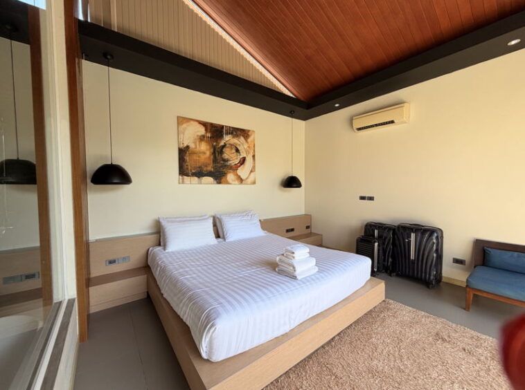 Hotel room with a king bed, white bedding, two pillows, and towels folded on the bed, flanked by pendant lamps.