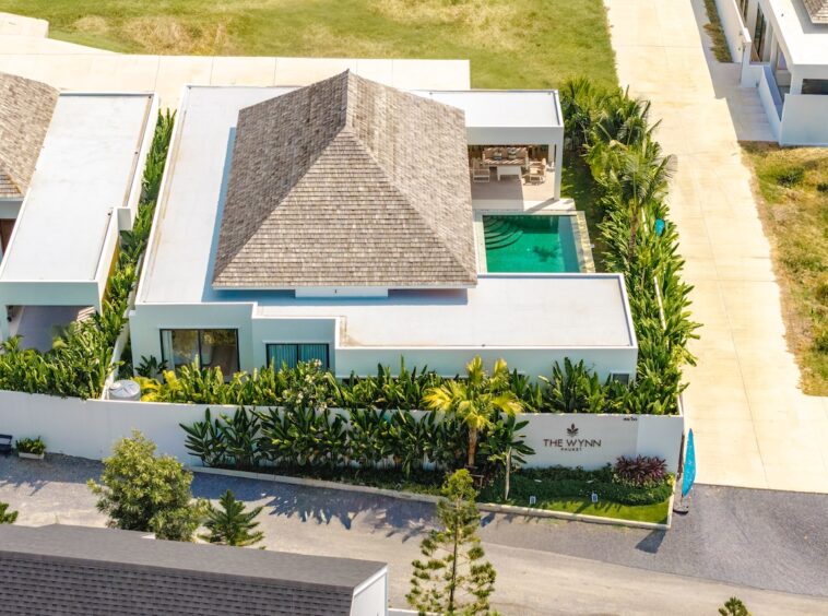 Aerial view of a modern villa with a central pyramid-shaped thatched roof, a rectangular pool, and tropical landscaping around The Wynn Phuket.