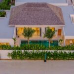 Aerial view of a modern villa with a central pool, surrounded by tropical plants and a white perimeter wall.
