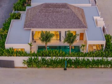 Aerial view of a modern villa with a central pool, surrounded by tropical plants and a white perimeter wall.