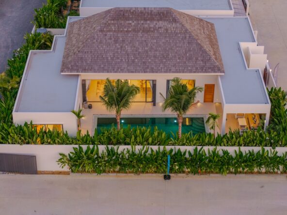 Aerial view of a modern villa with a central pool, surrounded by tropical plants and a white perimeter wall.
