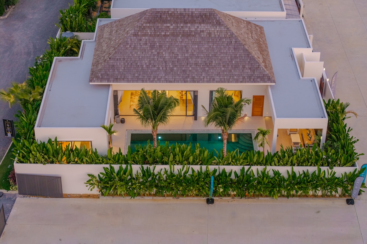 Aerial view of a modern villa with a central pool, surrounded by tropical plants and a white perimeter wall.