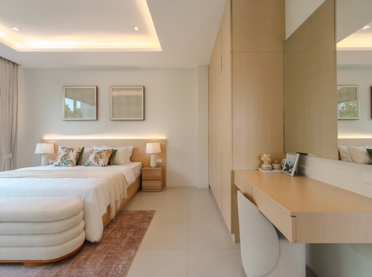 Bright hotel bedroom with a large bed, two nightstands, and a curved white ottoman at the foot of the bed.