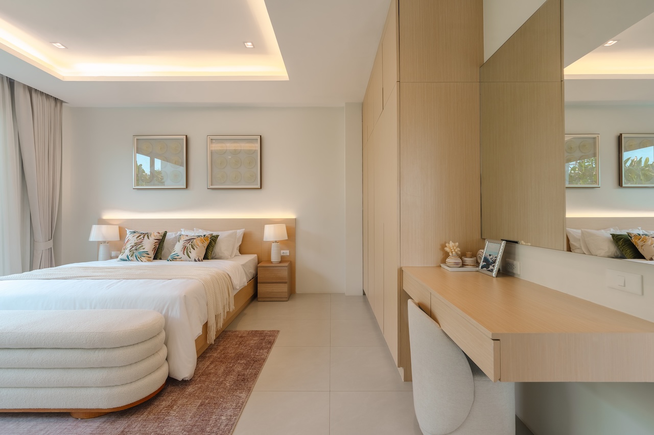 Bright hotel bedroom with a large bed, two nightstands, and a curved white ottoman at the foot of the bed.