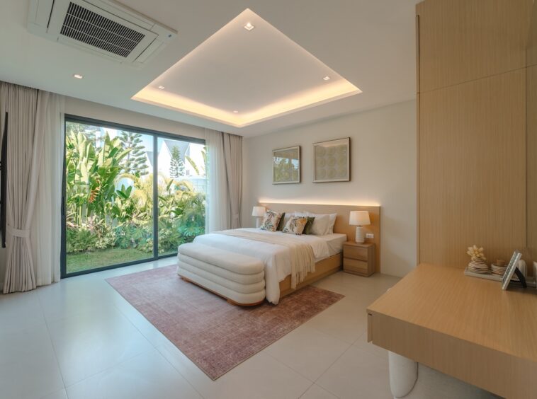 Bright hotel bedroom with a king bed, two nightstands, lamps, and a sliding glass door to a tropical garden outside.
