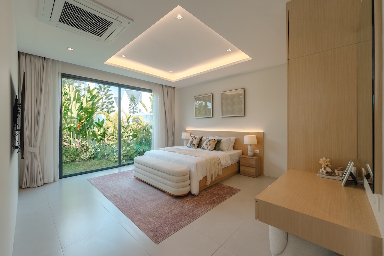 Bright hotel bedroom with a king bed, two nightstands, lamps, and a sliding glass door to a tropical garden outside.