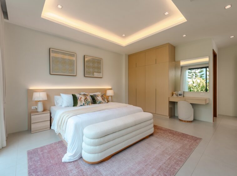 Bright modern bedroom with a king bed, two nightstands, matching lamps, a wood bench at the foot, and a large built-in wardrobe on the right.