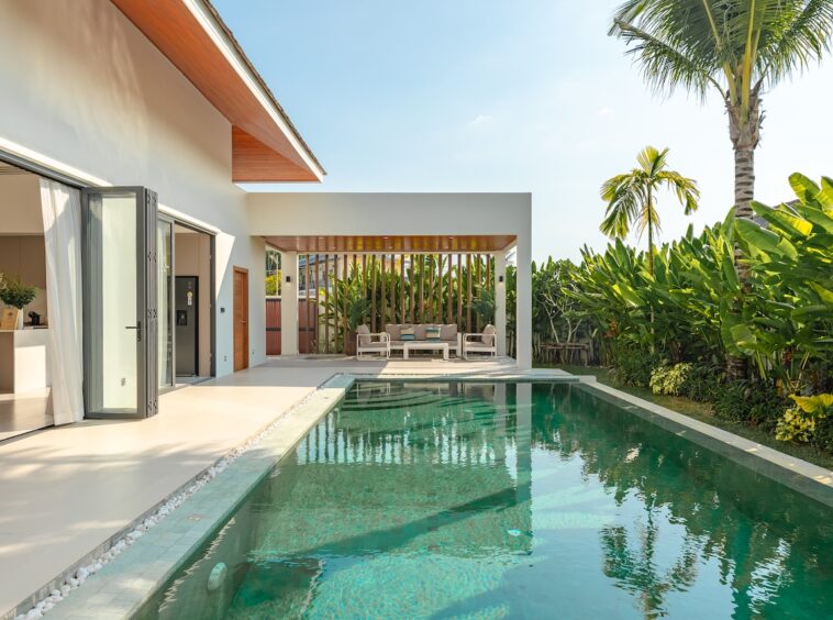 Modern villa with a rectangular pool, glass doors, and a shaded outdoor seating area on a sunny day