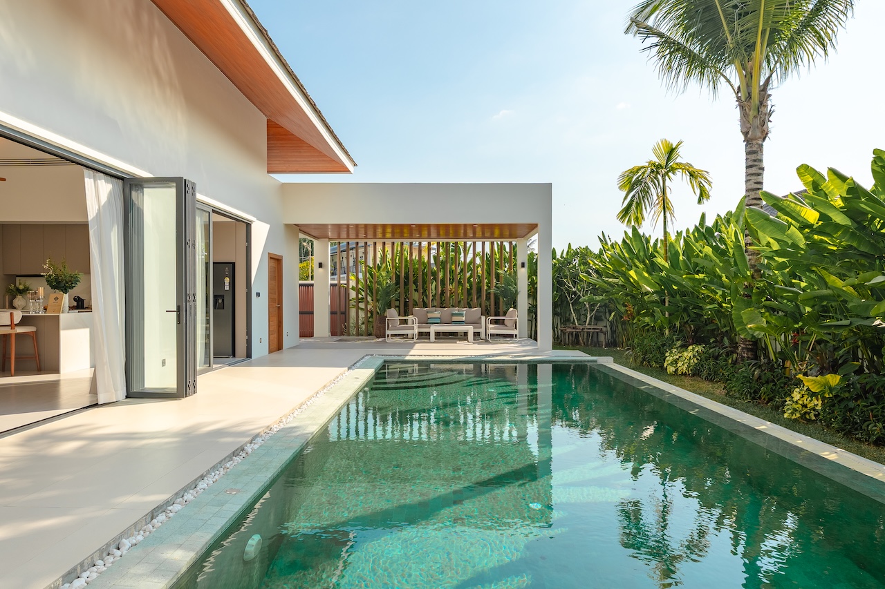 Modern villa with a rectangular pool, glass doors, and a shaded outdoor seating area on a sunny day