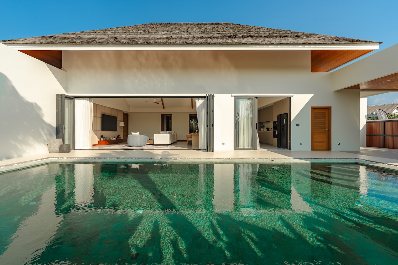 Modern house with a rectangular swimming pool in the foreground and open sliding doors leading to a bright living area.