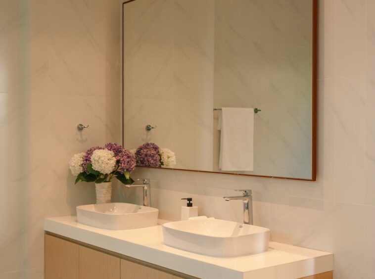 Modern bathroom with a double-sink vanity, white countertop, light wood cabinets, and a large framed mirror above.
