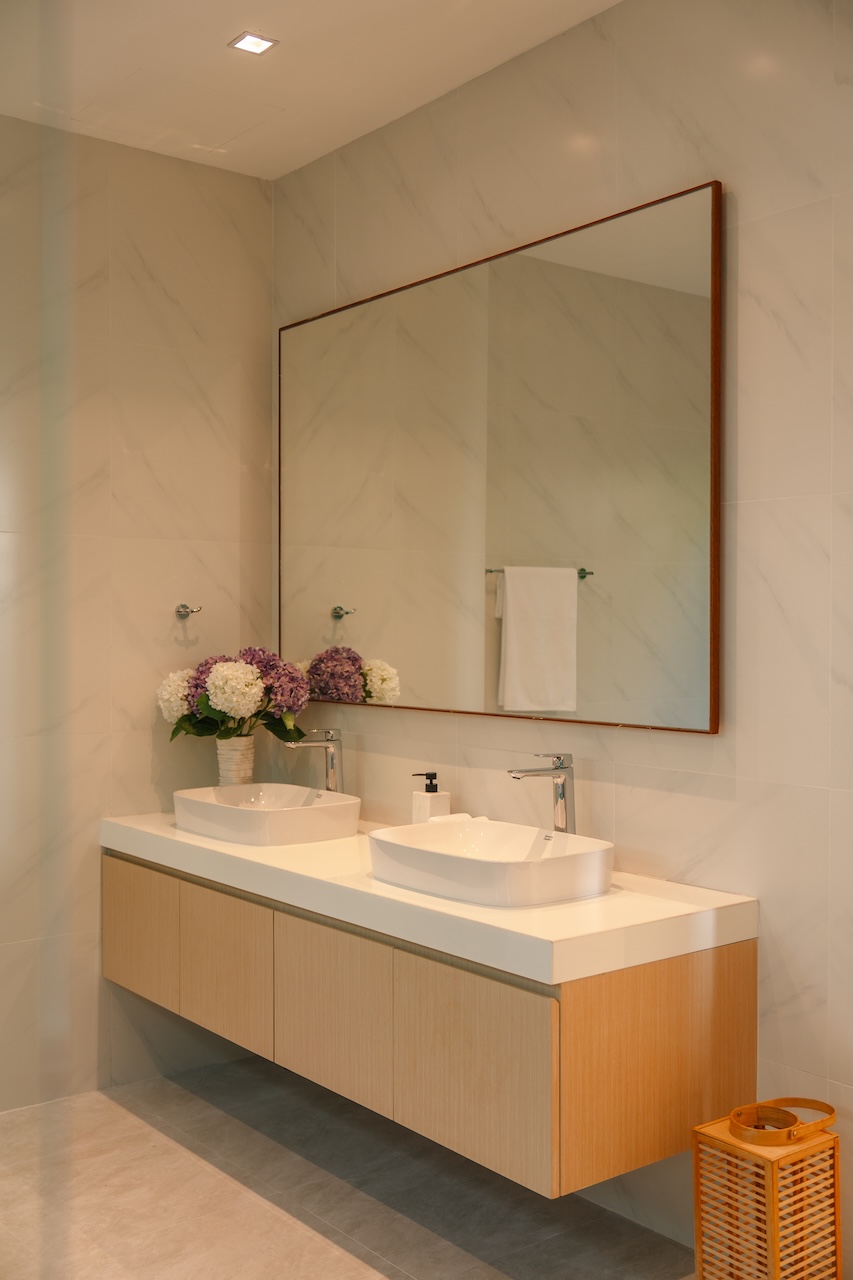 Modern bathroom with a double-sink vanity, white countertop, light wood cabinets, and a large framed mirror above.