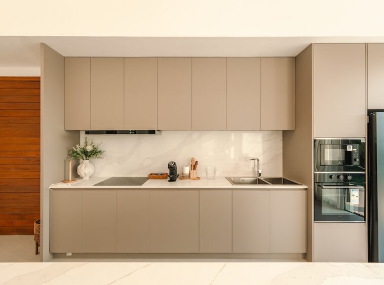 Modern beige kitchen with upper and lower cabinets, marble backsplash, and built‑in appliances on the right politely streamlined for a clean look.