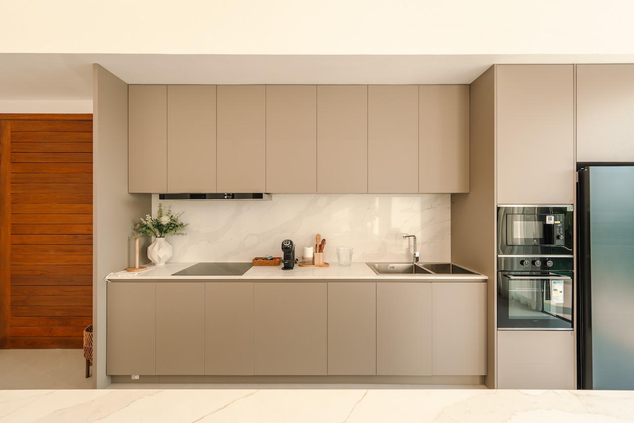 Modern beige kitchen with upper and lower cabinets, marble backsplash, and built‑in appliances on the right politely streamlined for a clean look.