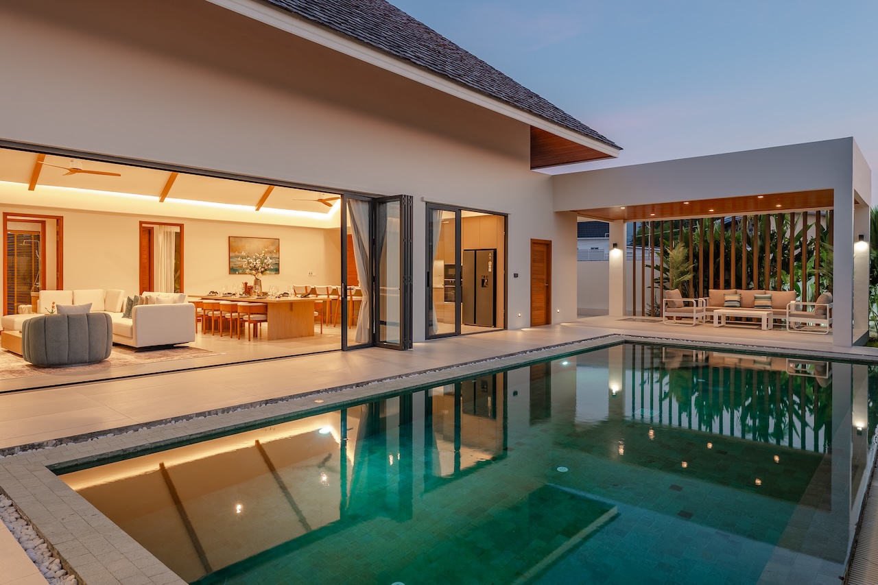 Modern villa with an open-plan living/dining area and a rectangular pool along the terrace at dusk.