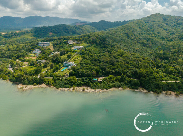 Aerial view of a green hillside coastline with scattered houses and a pool near the shore; Ocean Worldwide Real Estate logo bottom-right.