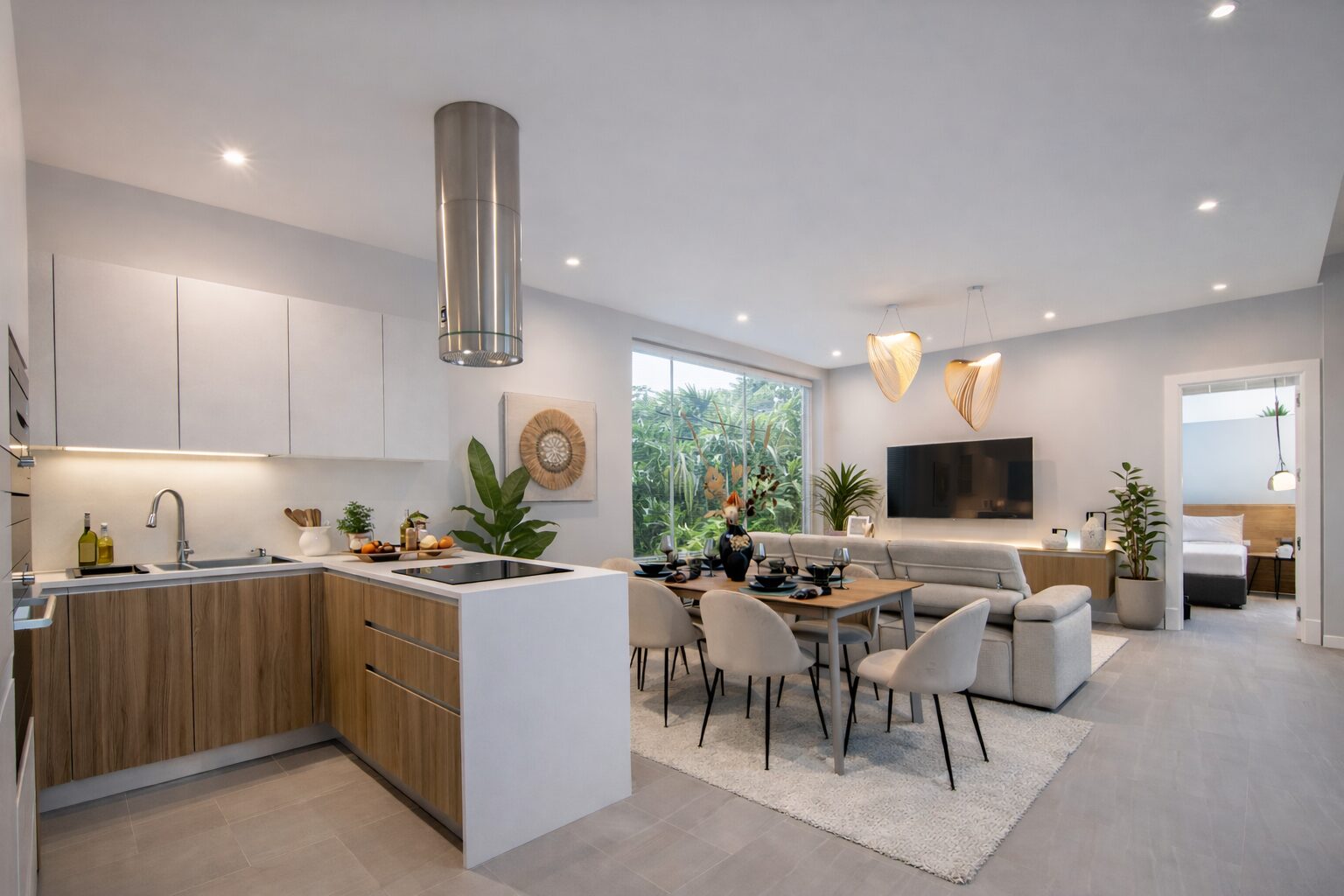 Open-plan kitchen, dining, and living space with a wood-toned island, white cabinets, and a grey sectional facing a wall-mounted TV.