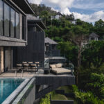 Modern hillside resort with glass-walled balconies and a poolside terrace overlooking lush greenery.