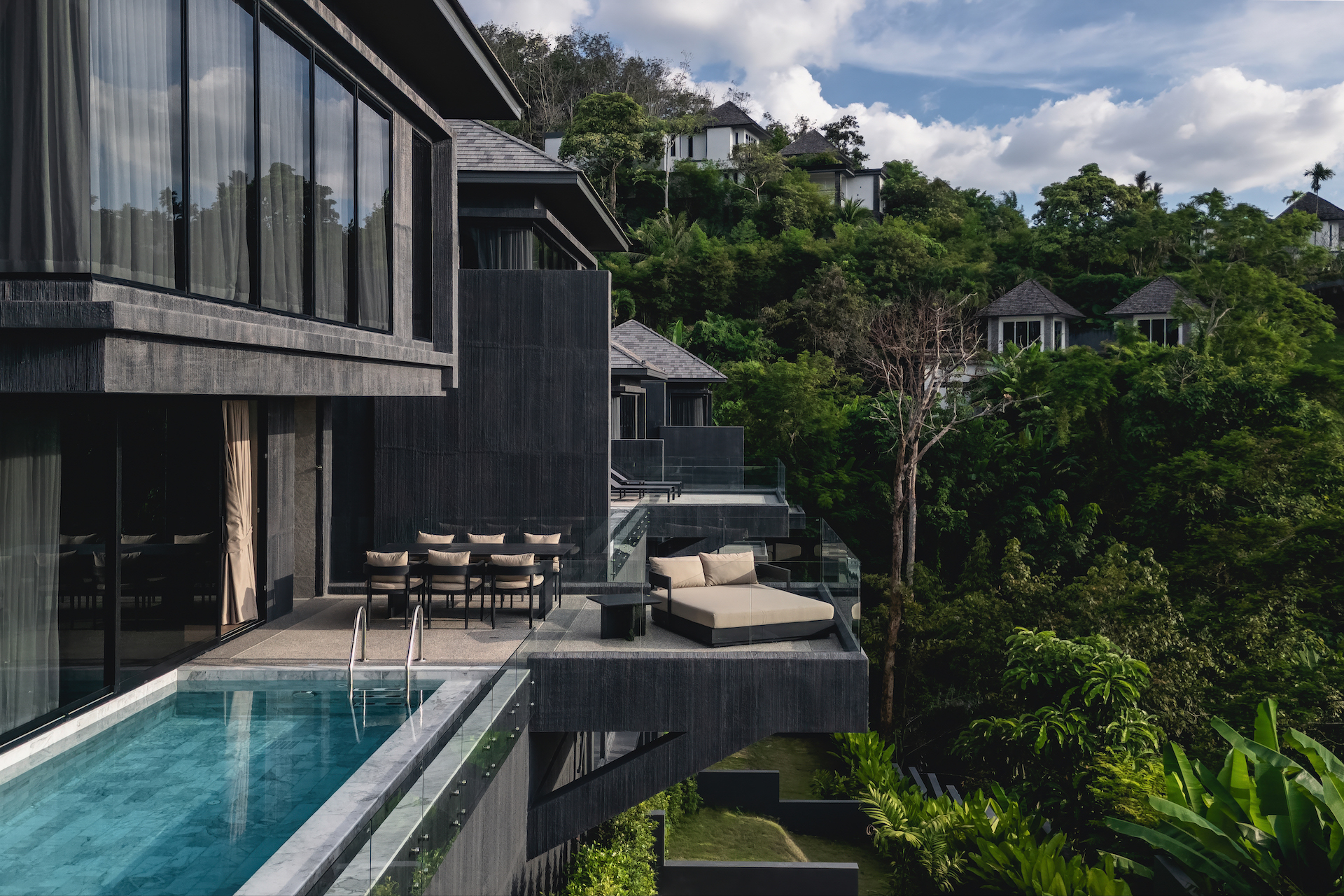 Modern hillside resort with glass-walled balconies and a poolside terrace overlooking lush greenery.