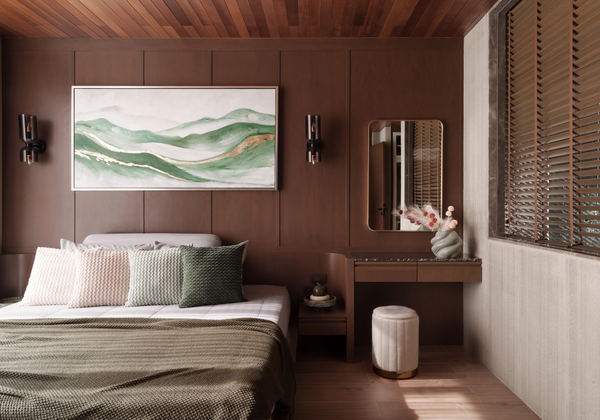 Wood-paneled bedroom with a green landscape painting, two wall lamps, and a mirror on the right side.