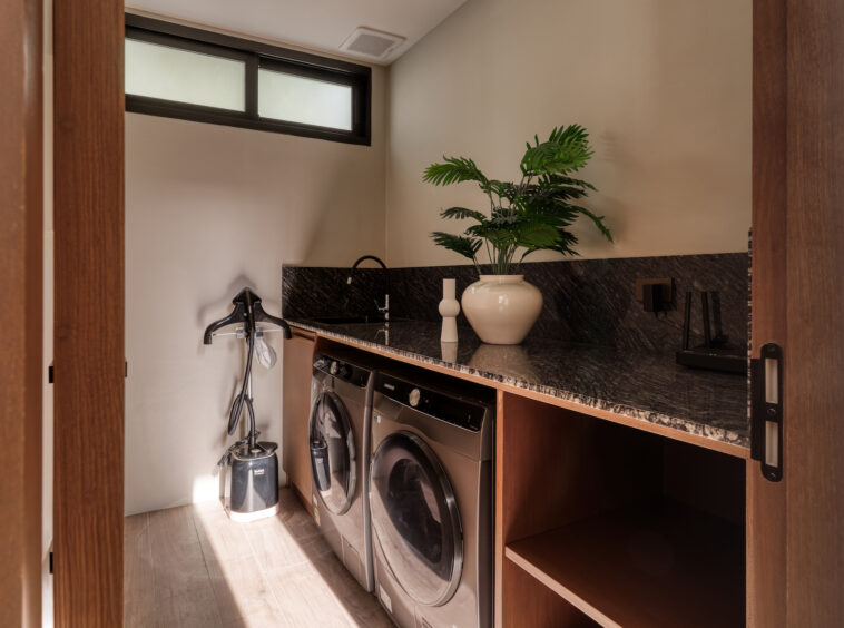 Laundry room with a black granite counter, front-loading washer and dryer, and a large potted plant near a window.
