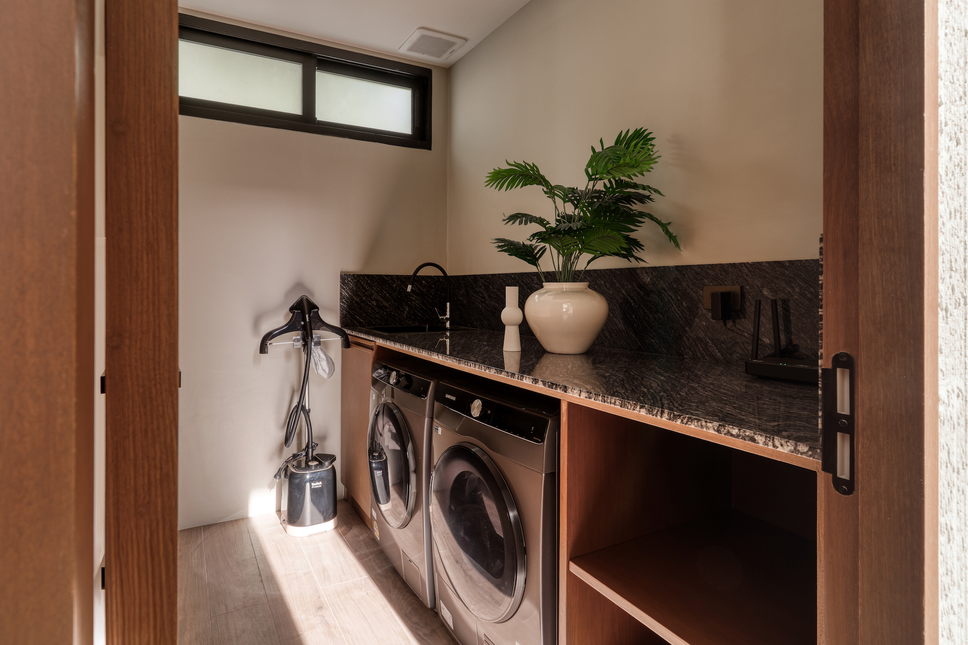 Laundry room with a black granite counter, front-loading washer and dryer, and a large potted plant near a window.
