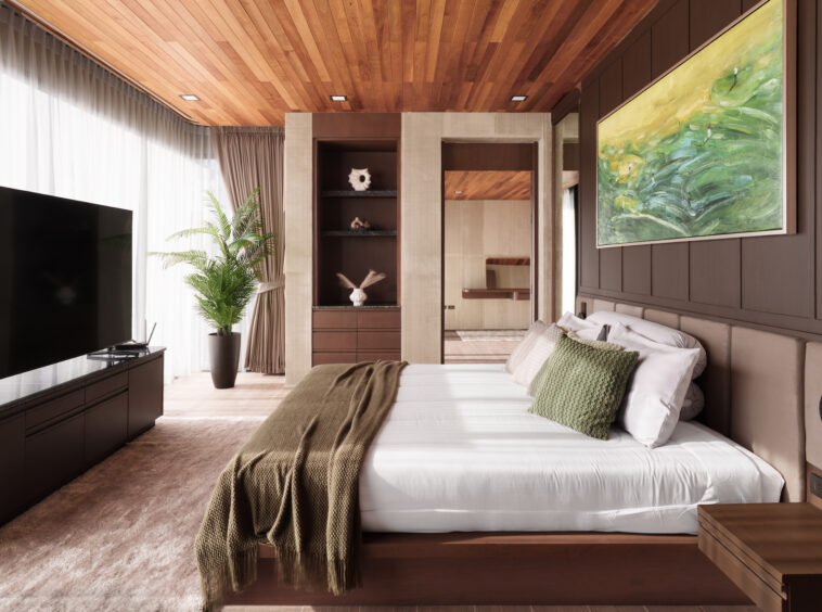 Hotel bedroom with a low wood platform bed, green throw pillows, and a large abstract painting on a brown paneled wall.