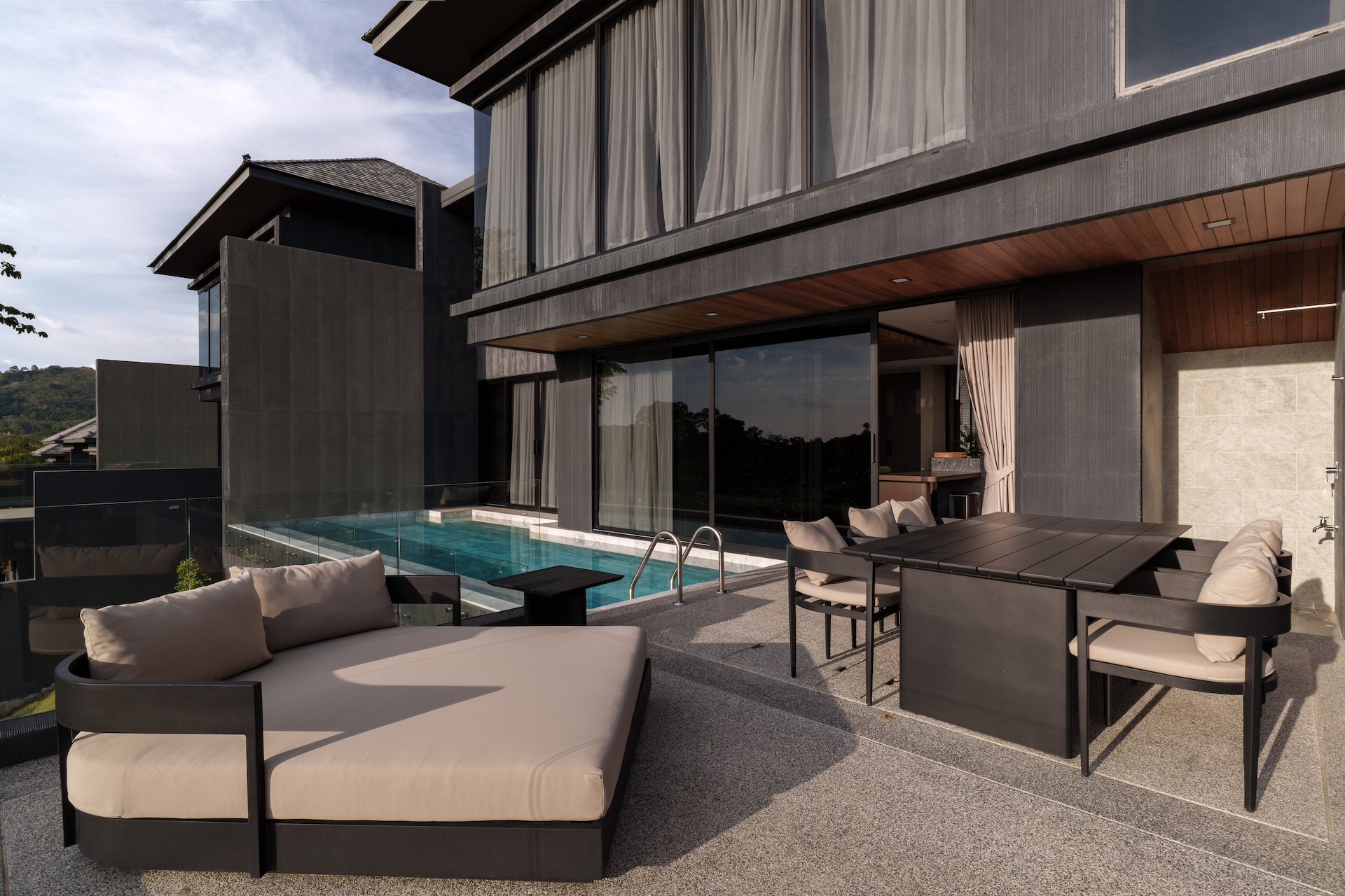 Modern outdoor lounge beside a rectangular pool on a glass-railed terrace with large windows and dark exterior.