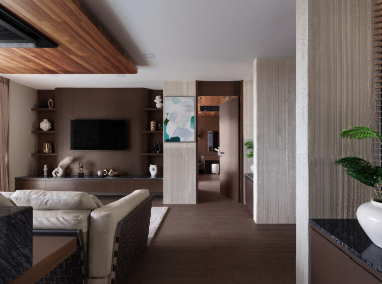 Modern living room with brown wood accents, built‑in shelves, and a wall‑mounted TV with decorative objects on shelves.