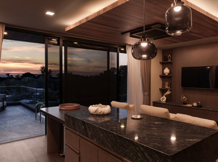 Modern kitchen with a dark granite island, pendant lights, and a sunset view through sliding glass doors to a balcony.
