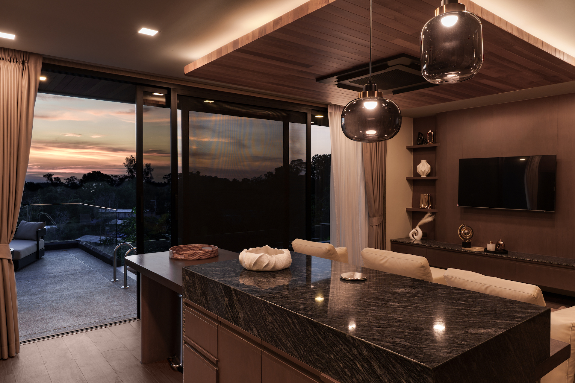 Modern kitchen with a dark granite island, pendant lights, and a sunset view through sliding glass doors to a balcony.