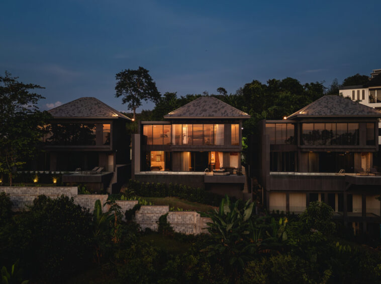 Luxury glass-fronted villas at dusk with warm interior lighting and tropical landscaping