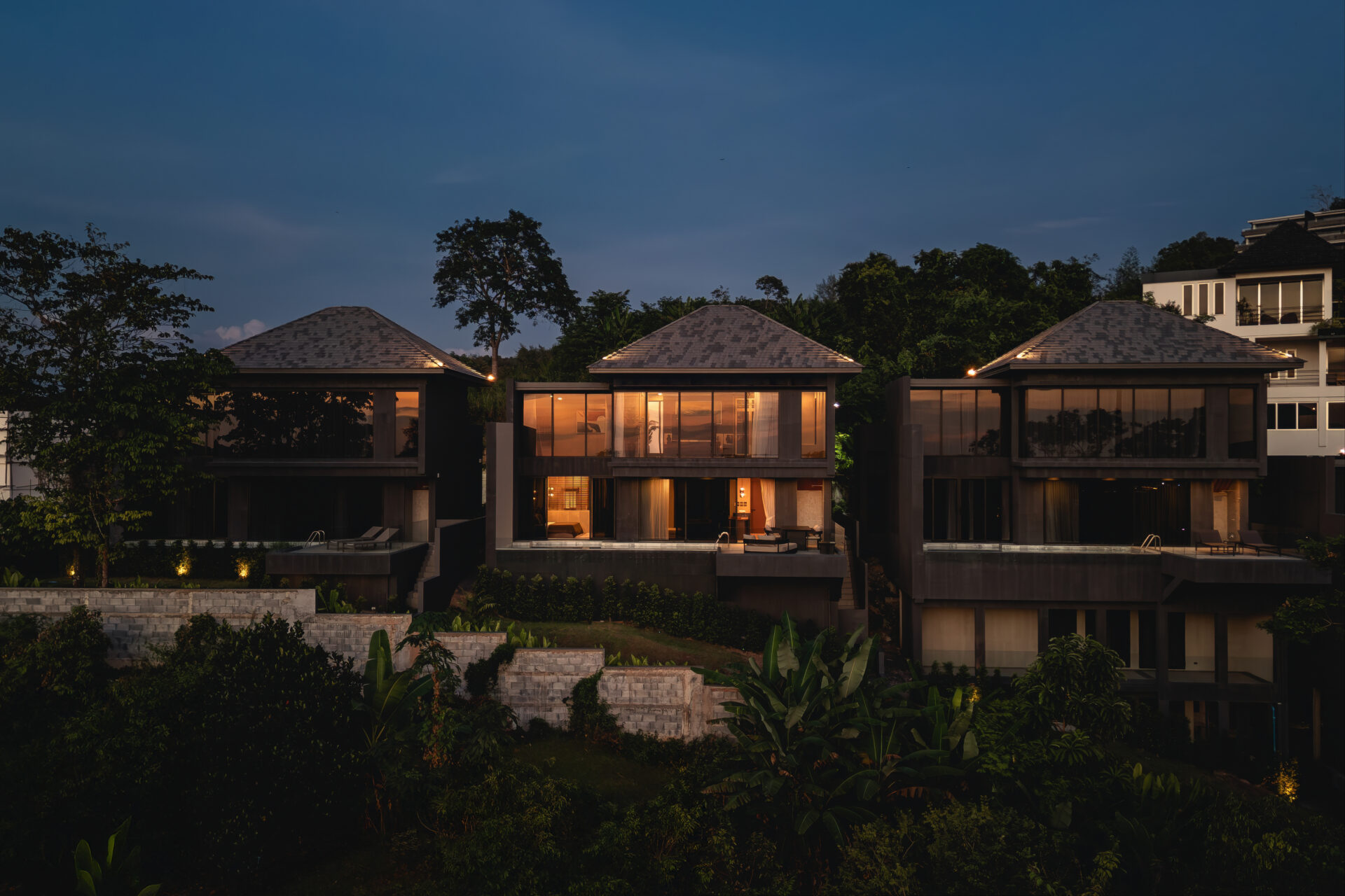 Luxury glass-fronted villas at dusk with warm interior lighting and tropical landscaping