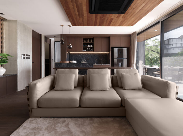 Open-plan living room with a beige sectional, dark wood kitchen, and glass doors to the patio.