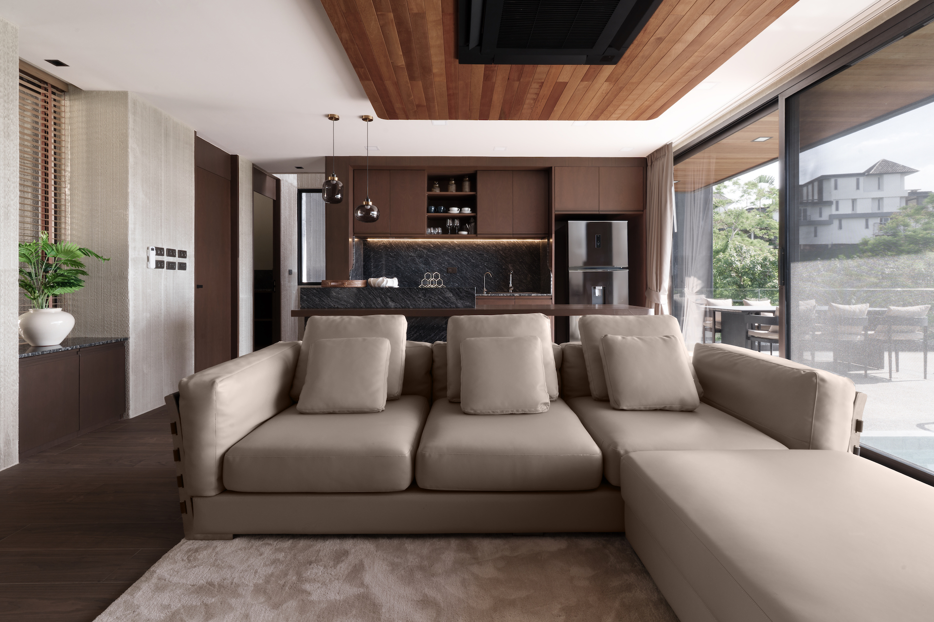 Open-plan living room with a beige sectional, dark wood kitchen, and glass doors to the patio.