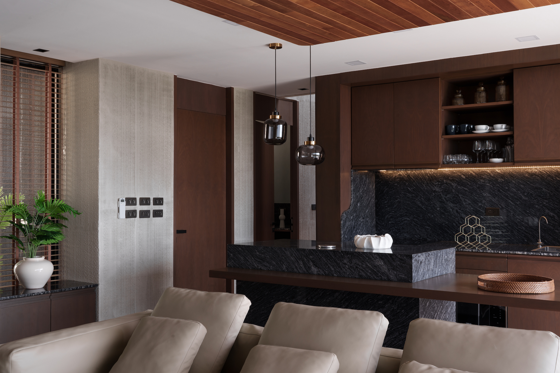 Open-plan kitchen and living area with dark wood cabinets, black marble island, and modern pendant lights.