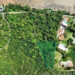 Aerial view of a forested hillside with a triangular land parcel outlined in green among houses and roads.