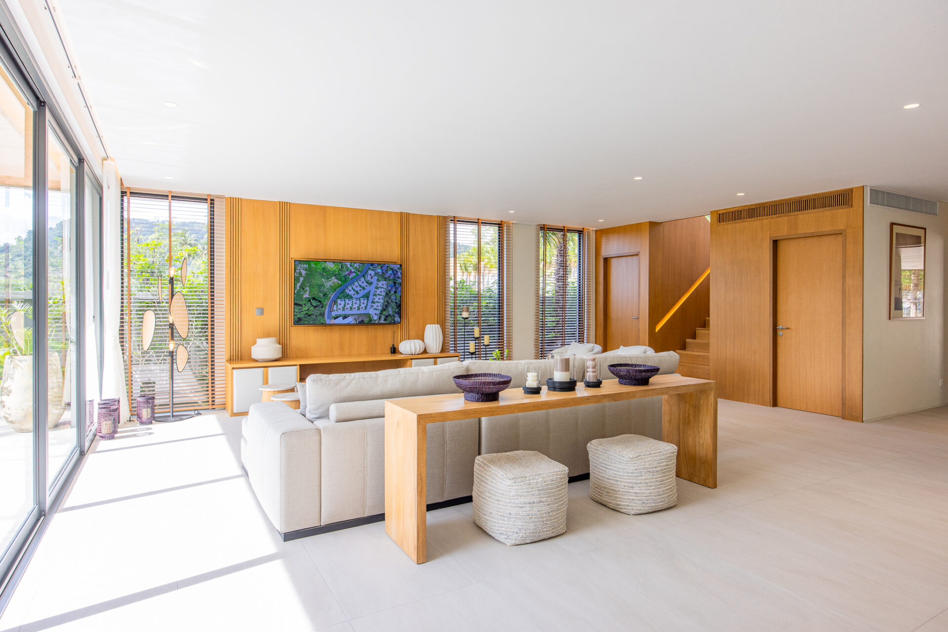 Bright open-concept living room with a beige sectional, wooden walls, and large glass doors to the outdoors. Whether informative or decorative, it conveys a spacious, sunlit living area.