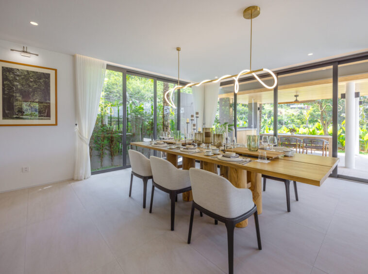 Bright dining room with a long wooden table set for a meal, white upholstered chairs, and a sculptural wavy pendant light above.