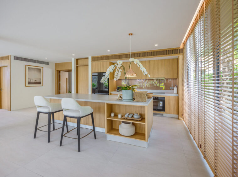 Modern kitchen with a central island, three cream stools, and large wooden‑louvered windows','Open-plan kitchen featuring oak cabinets, built-in oven, and an orchid on the island' ,
