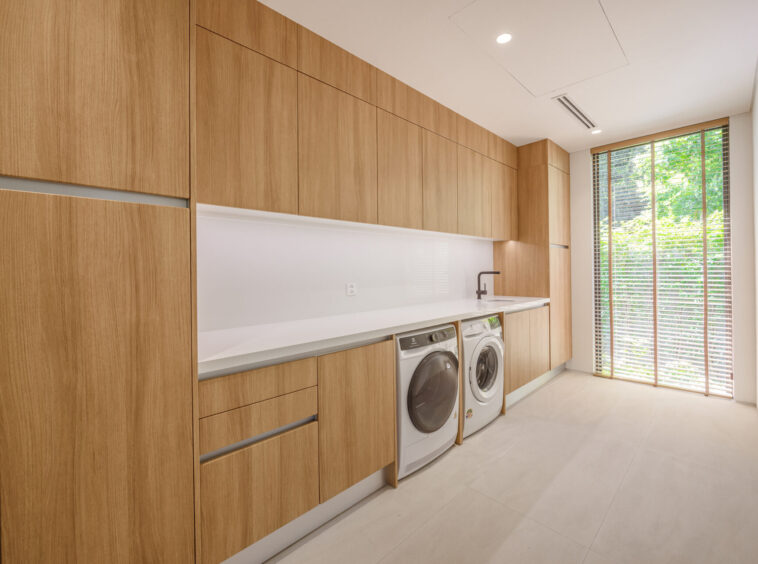 Modern laundry room with floor-to-ceiling oak cabinets, and a white countertop over front-loading washer and dryer.