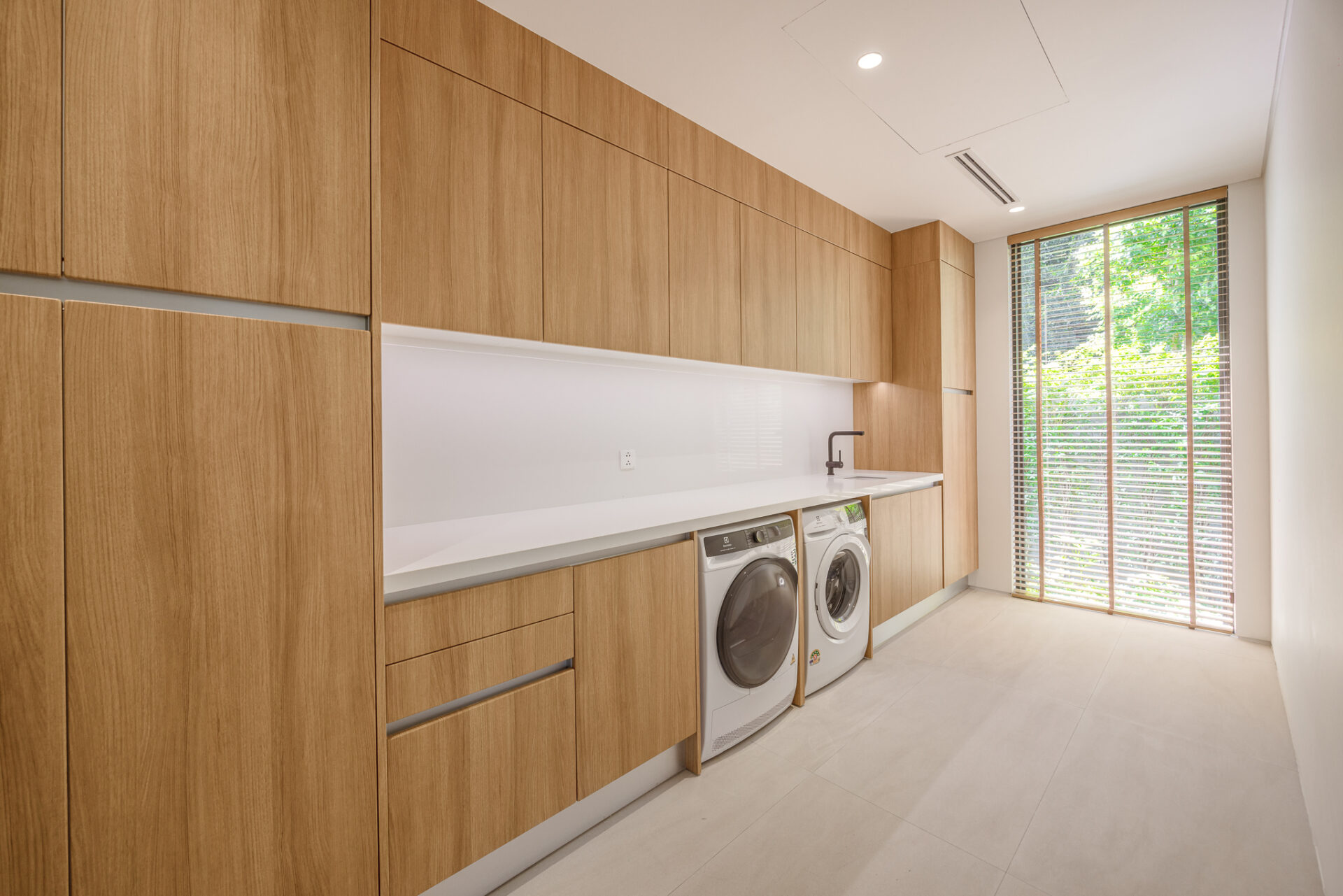 Modern laundry room with floor-to-ceiling oak cabinets, and a white countertop over front-loading washer and dryer.