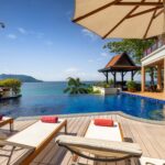 Luxury resort pool deck with lounge chairs and red towels, overlooking the ocean and distant island under a clear blue sky.