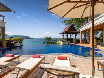 Luxury resort pool deck with lounge chairs and red towels, overlooking the ocean and distant island under a clear blue sky.
