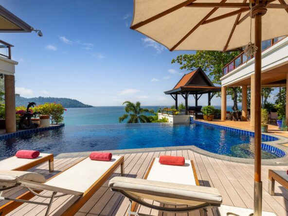 Luxury resort pool deck with lounge chairs and red towels, overlooking the ocean and distant island under a clear blue sky.