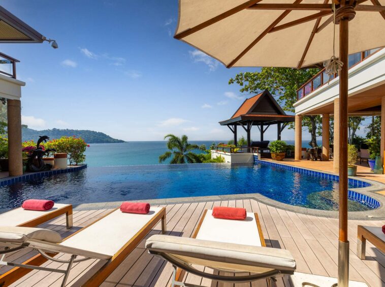 Luxury resort pool deck with lounge chairs and red towels, overlooking the ocean and distant island under a clear blue sky.