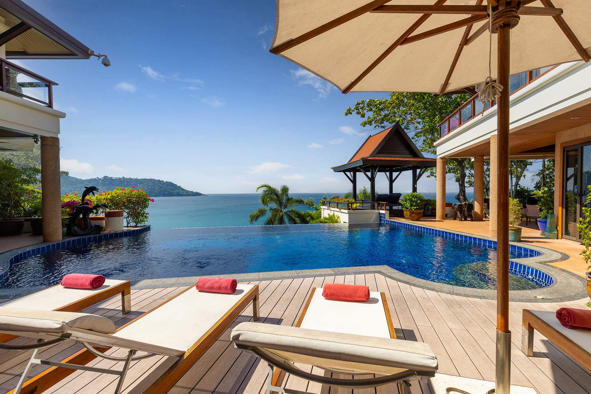 Luxury resort pool deck with lounge chairs and red towels, overlooking the ocean and distant island under a clear blue sky.