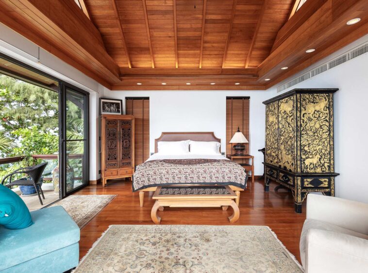 Bedroom with a wood-paneled ceiling, large bed at center, and antique carved cabinets on both sides; sliding glass doors open to a balcony on the left.